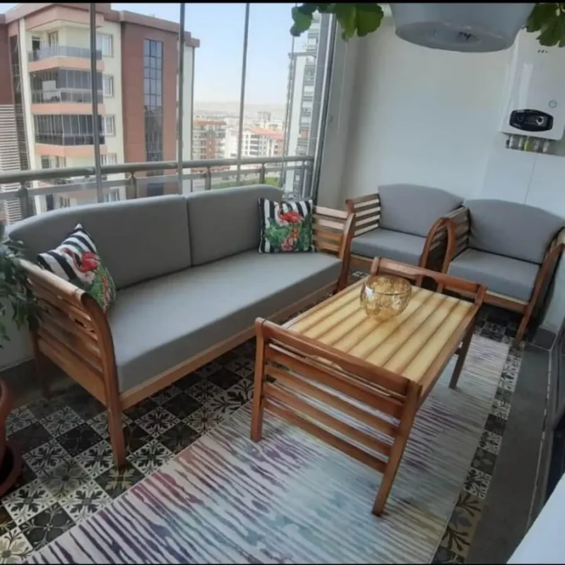 Cam balkon içinde doğal ahşap çerçeveli 2li koltuk ve 2 tekli koltuk takımı gri minderler ile dekore edilmiş