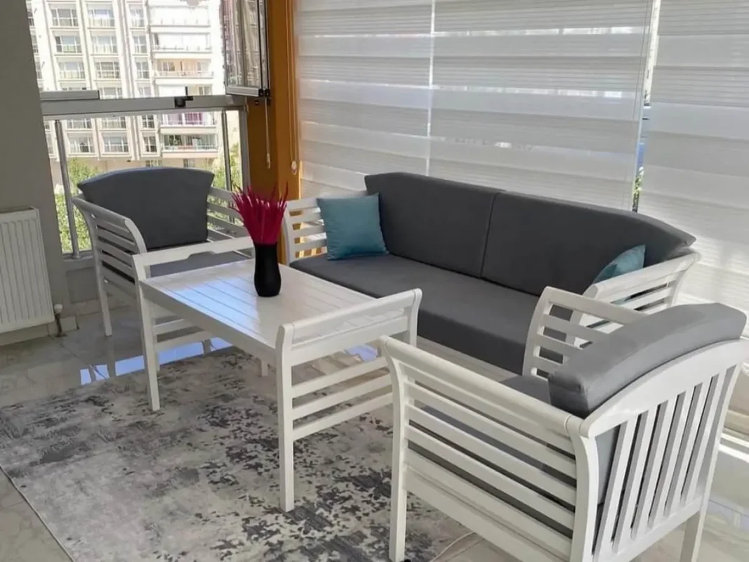Cam balkon içinde beyaz ahşap çerçeveli üçlü koltuk takımı gri minderler ile dekore edilmiş modern mobilya seti